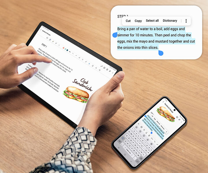 Człowiek klikający na Galaxy Tab A9+. Po prawej jest smartfon Galaxy. Oba urządzenia wyświetlają taki sam ekran. Część tekstu na smartfonie jest zaznaczona na niebiesko, aby wskazać funkcję kopiuj wklej pomiędzy urządzeniami. Nad urządzeniami jest powiększony, zaznaczony tekst, z opcjami zaznacz cały, wytnij, kopiuj, udostępnij i więcej.