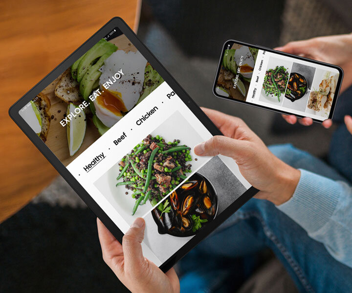 Dwie osoby siedzą obok siebie. Osoba po lewej trzyma Galaxy Tab A9+, a osoba po prawej trzyma smartfon Galaxy. Oba urządzenia wyświetlają taką samą witrynę o tematyce kulinarnej.